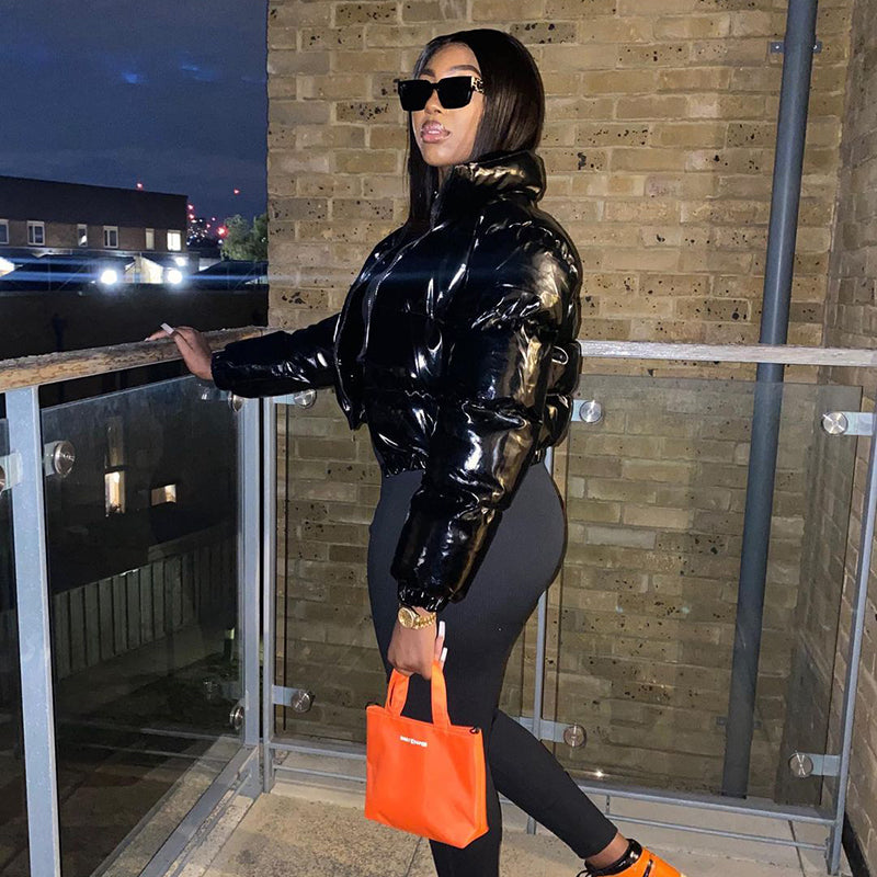 Stylish woman wearing a cropped shiny puffer coat paired with black leggings and an orange handbag
