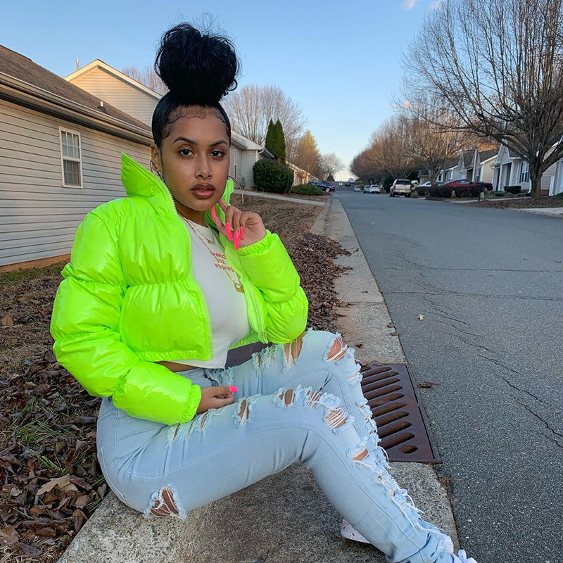 Model wearing a cropped shiny puffer coat in neon green, styled with distressed jeans for a trendy look