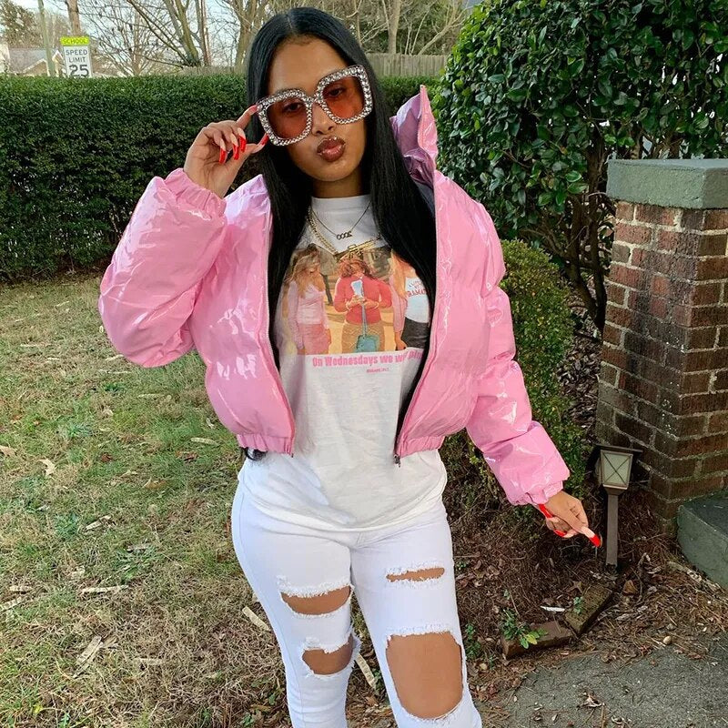 Stylish woman wearing a cropped shiny puffer coat in pink with oversized sunglasses and ripped jeans