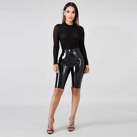 Model wearing patent leather bicycle shorts paired with a sheer black top for a stylish look